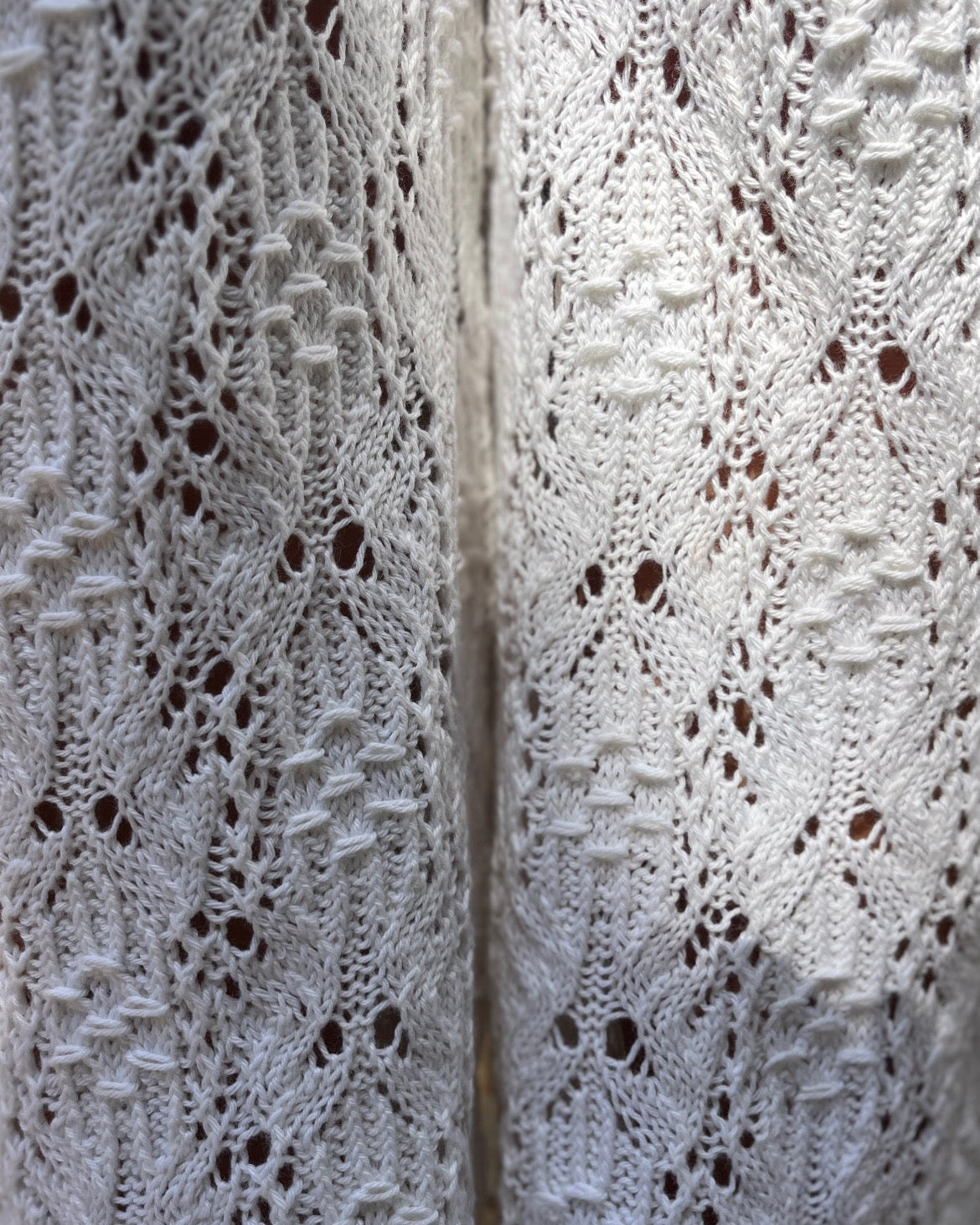 Close-up of a white lace smock panel with an intricate floral eyelet pattern, showing the texture and a central seam of the pants