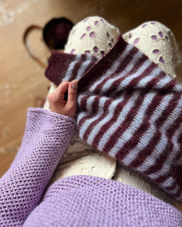 Model holding maroon and gray striped knitted polo sweater