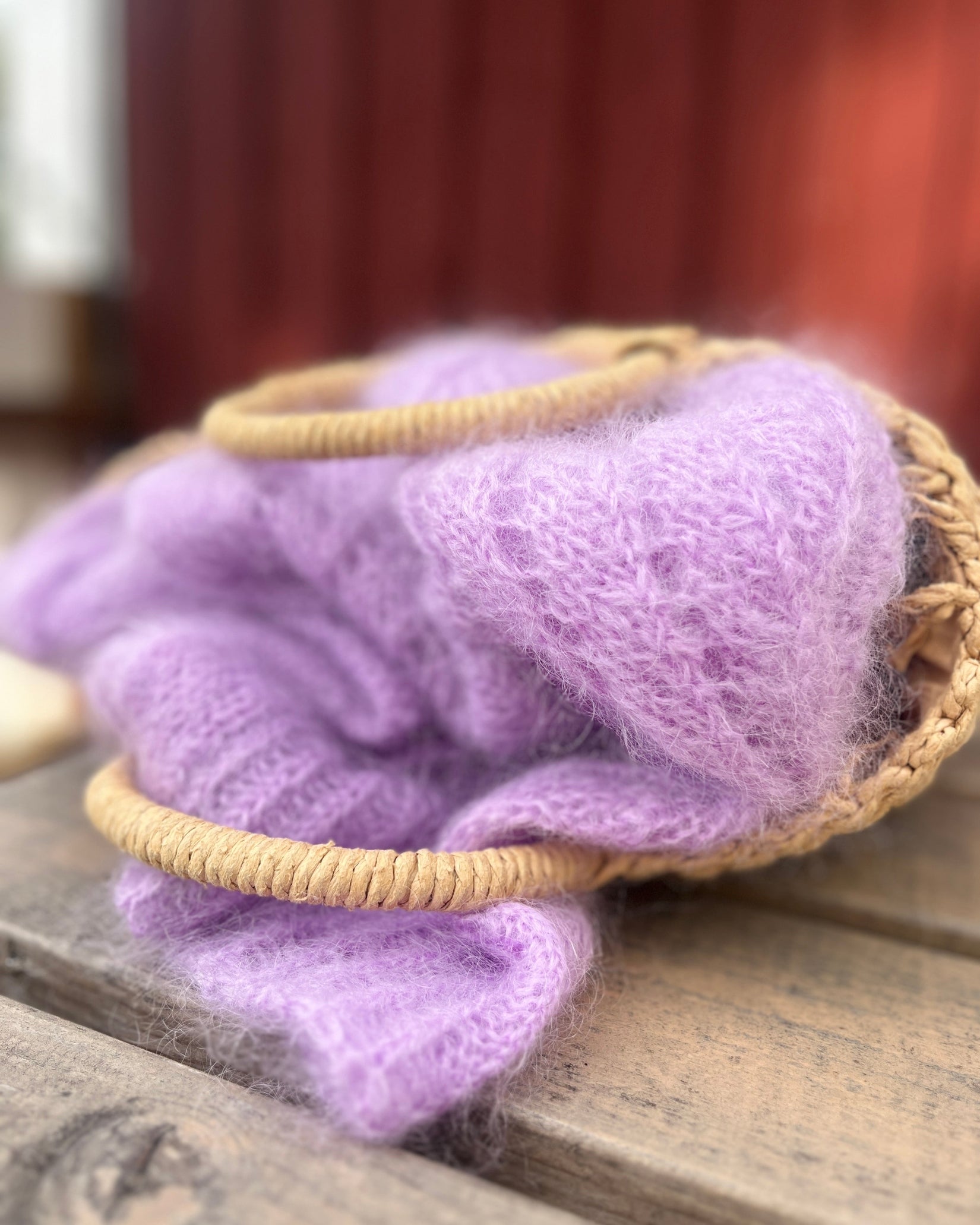 Lavender purple mohair knit cardigan draped over a small woven straw basket on a rustic wooden surface.