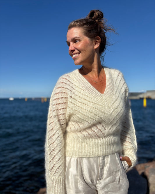 Cream fuzzy knit sweater with deep V-neck and flared sleeves worn outdoors