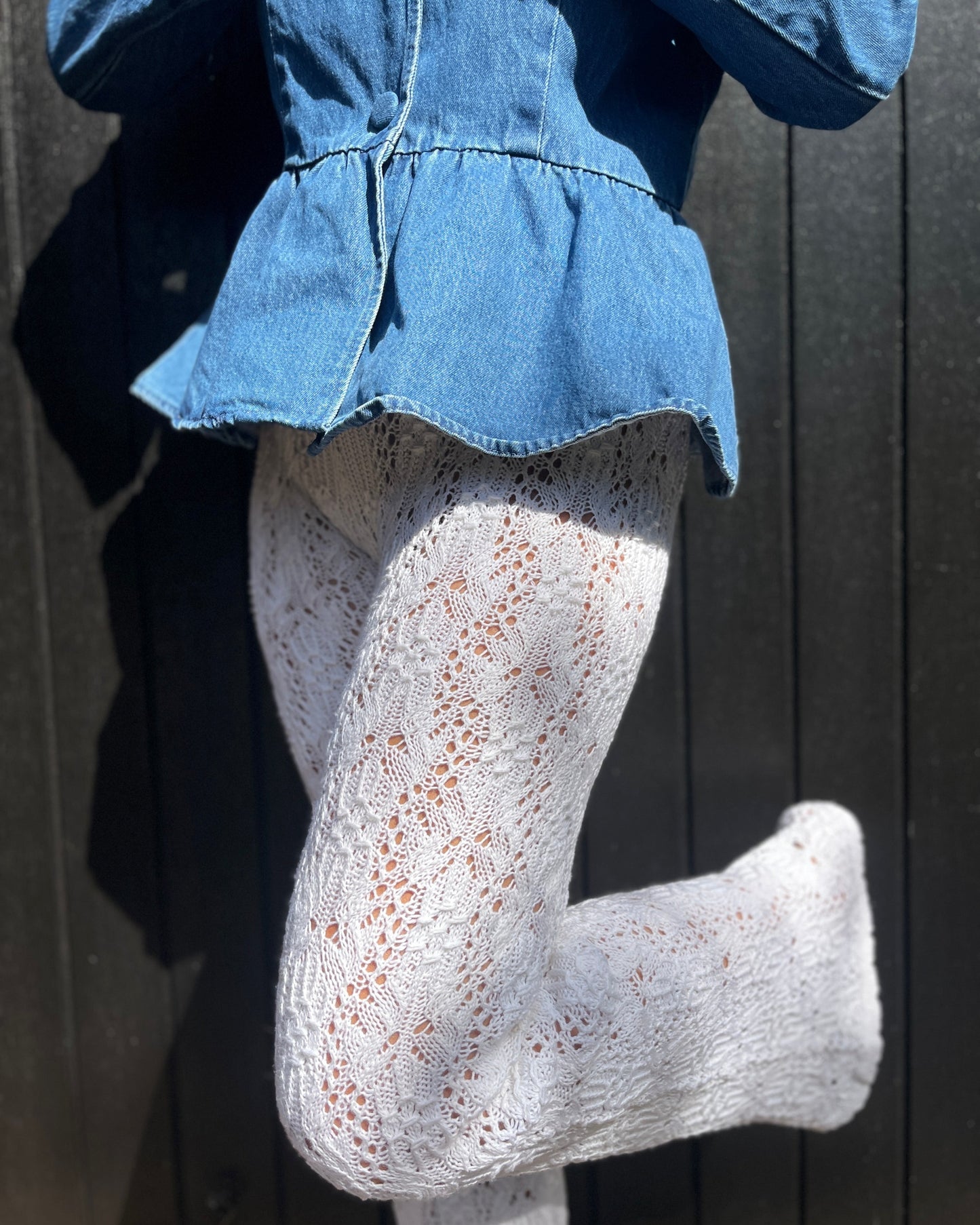 White lace and smock knit tights w, worn by a model in a blue denim top against a dark wooden background.
