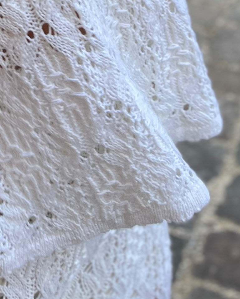 Close-up of a white eyelet lace fabric with a textured knit border, draped over a neutral stone surface.