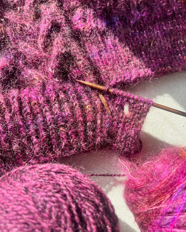 Close-up of pink yarn being knitted with a needle on a white background