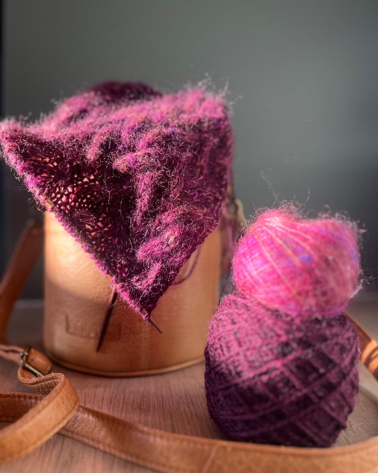 Purple knitted item and yarn on a wooden surface with a dark background