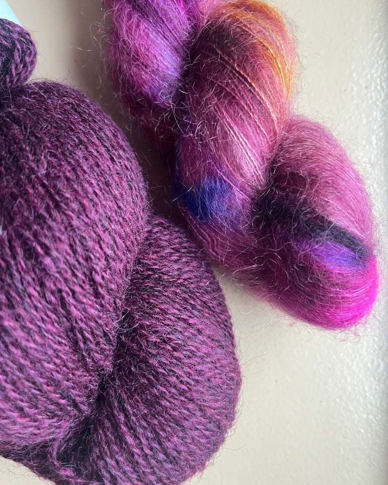 Two skeins of purple yarn with a gradient effect on a light background