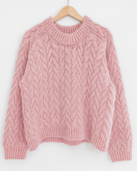 Pink cable knit sweater on a wooden hanger against a white background