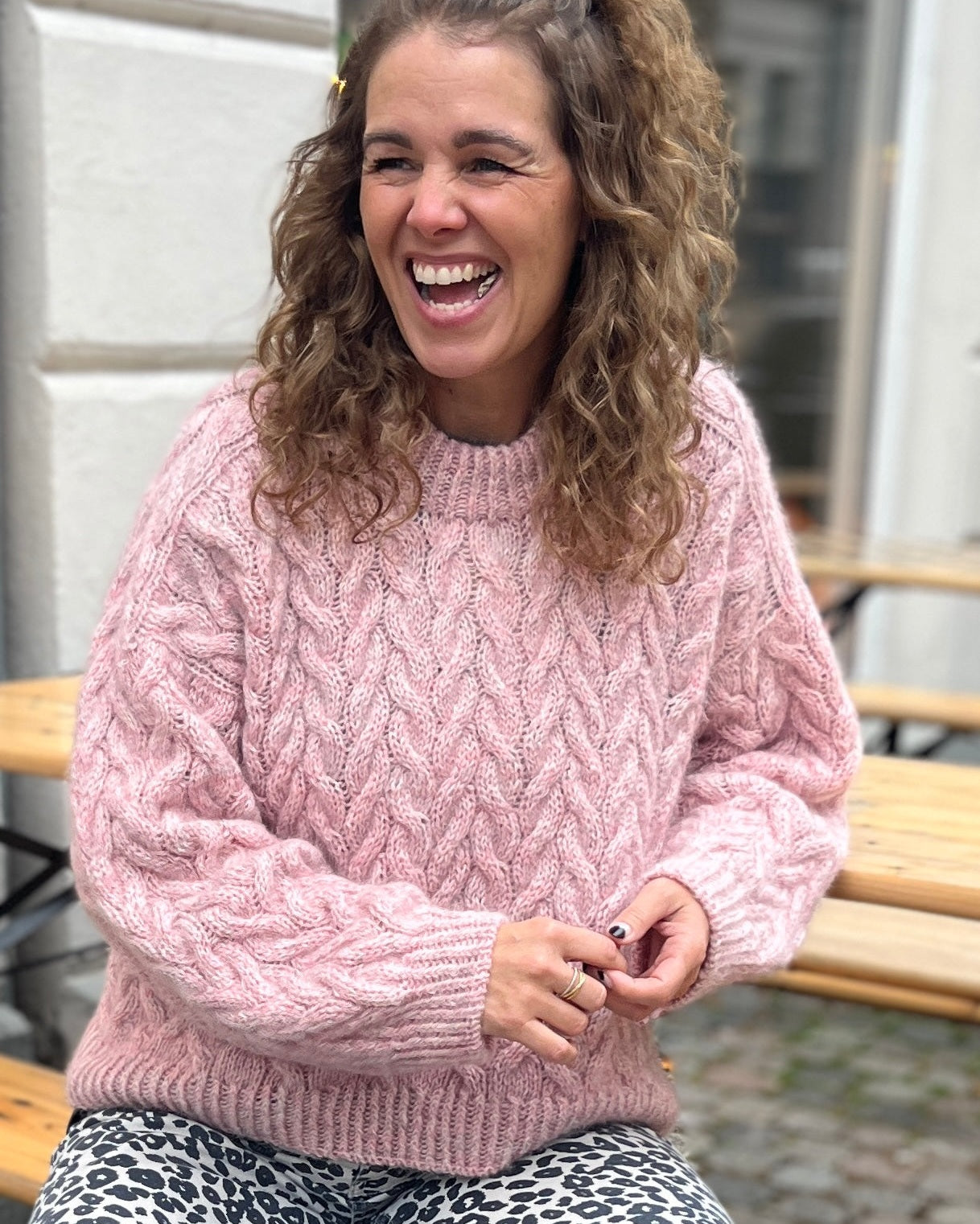 Person wearing a pink sweater sitting on a bench outdoors