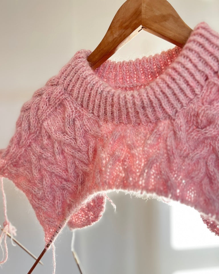 Pink knitted sweater on a wooden hanger against a white background