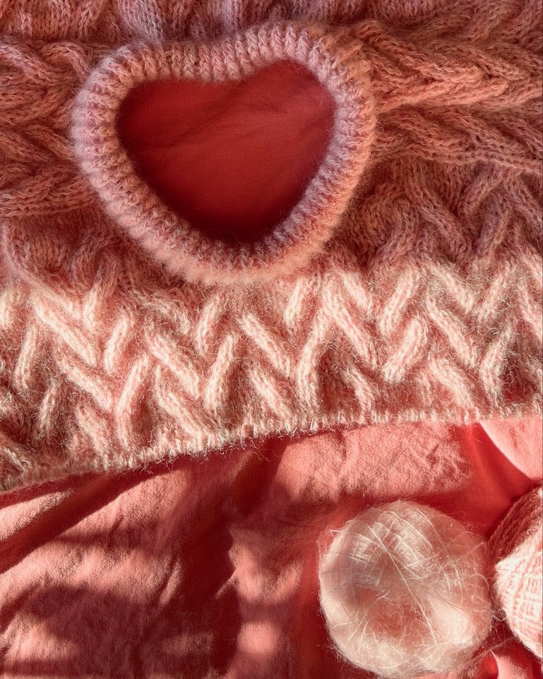Close-up of a knitted fabric with a heart-shaped opening and a pink yarn ball.
