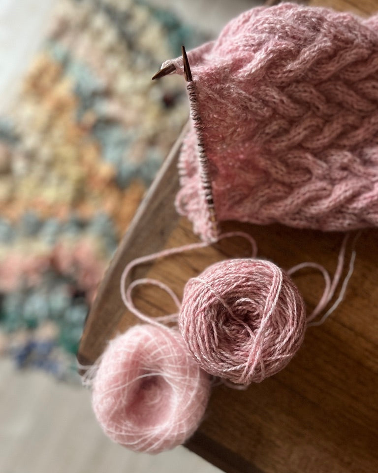 Pink yarn and knitting needles on a wooden surface with a blurred colorful pattern in the background