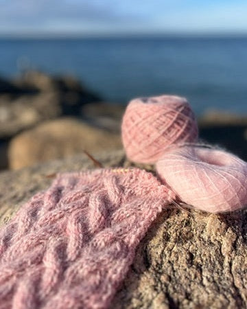 Pink knitted fabric on a rock with a blurred ocean background
